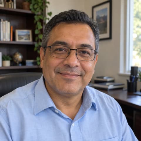Smiling man with glasses in a home office setting with books and plants.